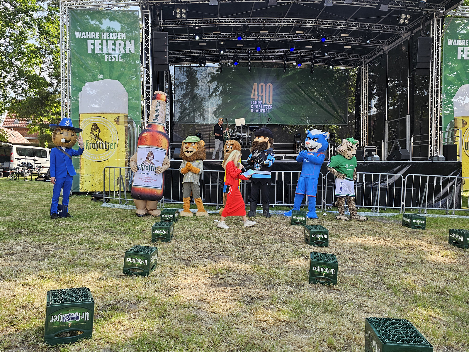 Kostümierte Maskottchen stehen vor einer Bühne auf einer Veranstaltung.