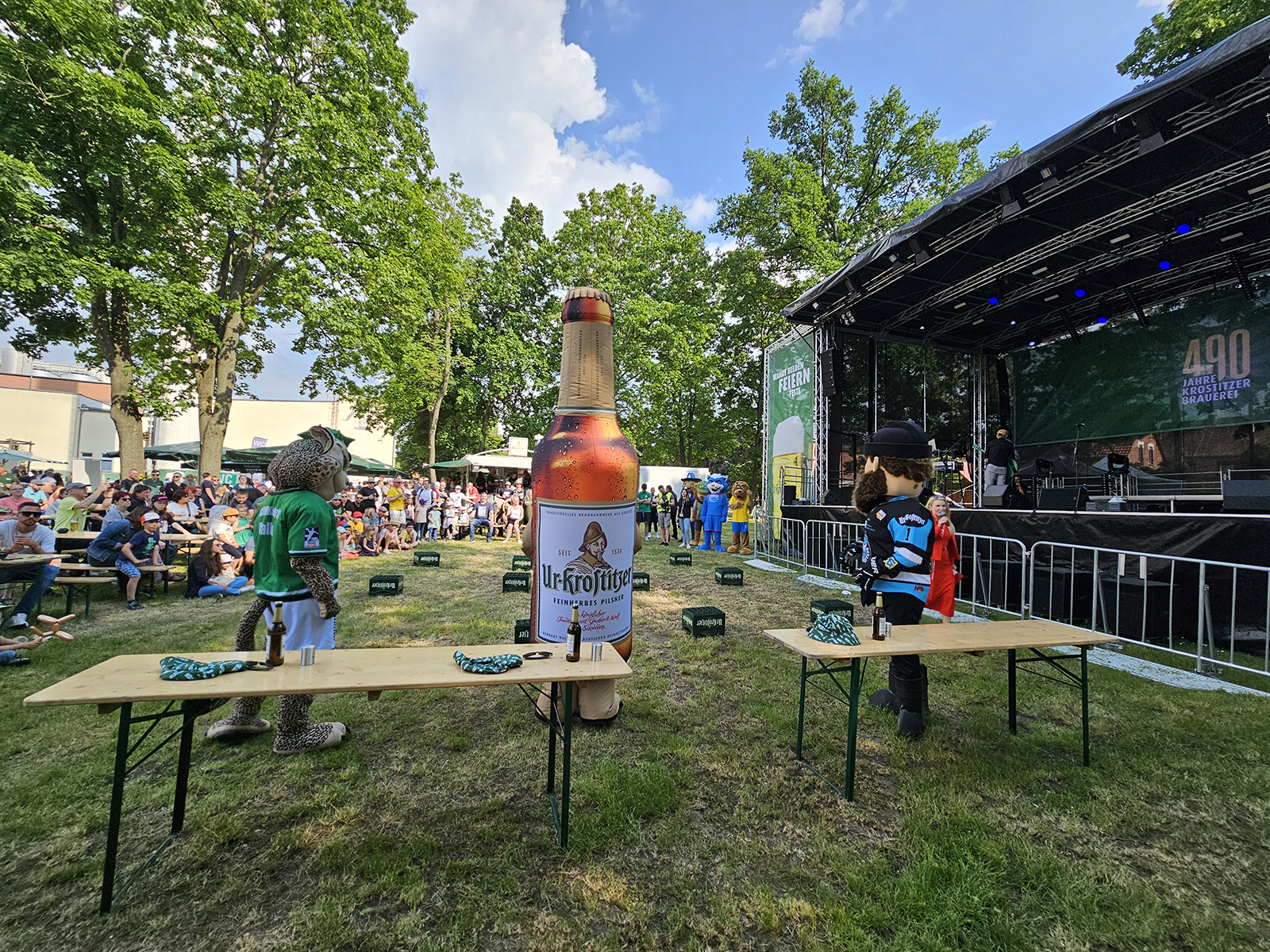 Personen beobachten eine Live-Bühne und Maskottchen bei einem Outdoor-Event.