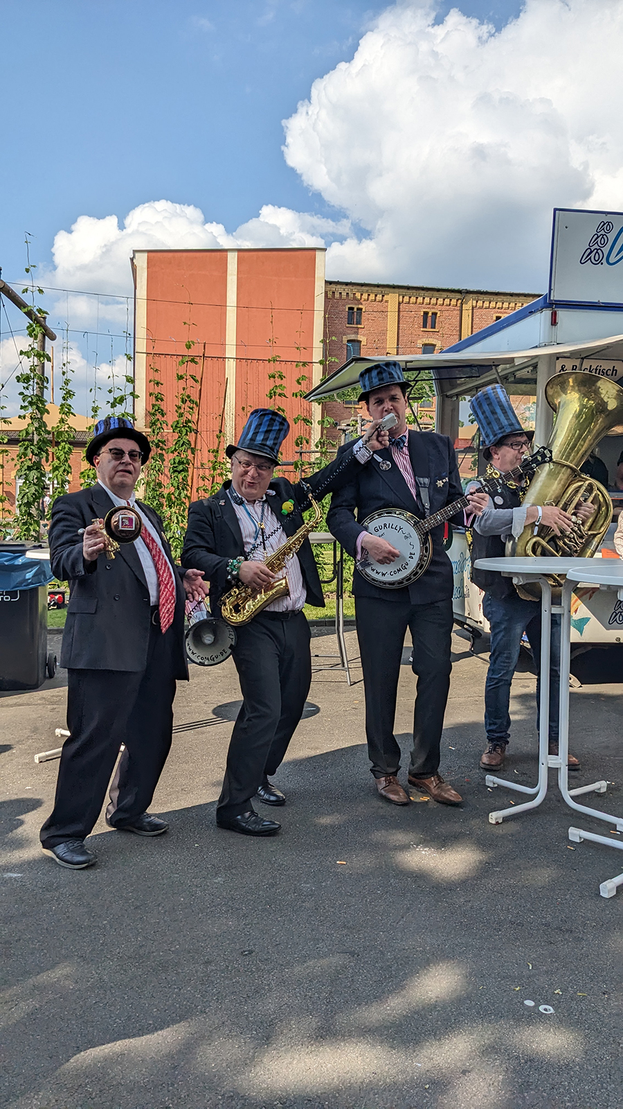 Drei Musiker in Anzügen spielen Saxophon, Banjo und Tuba auf einer Straße.