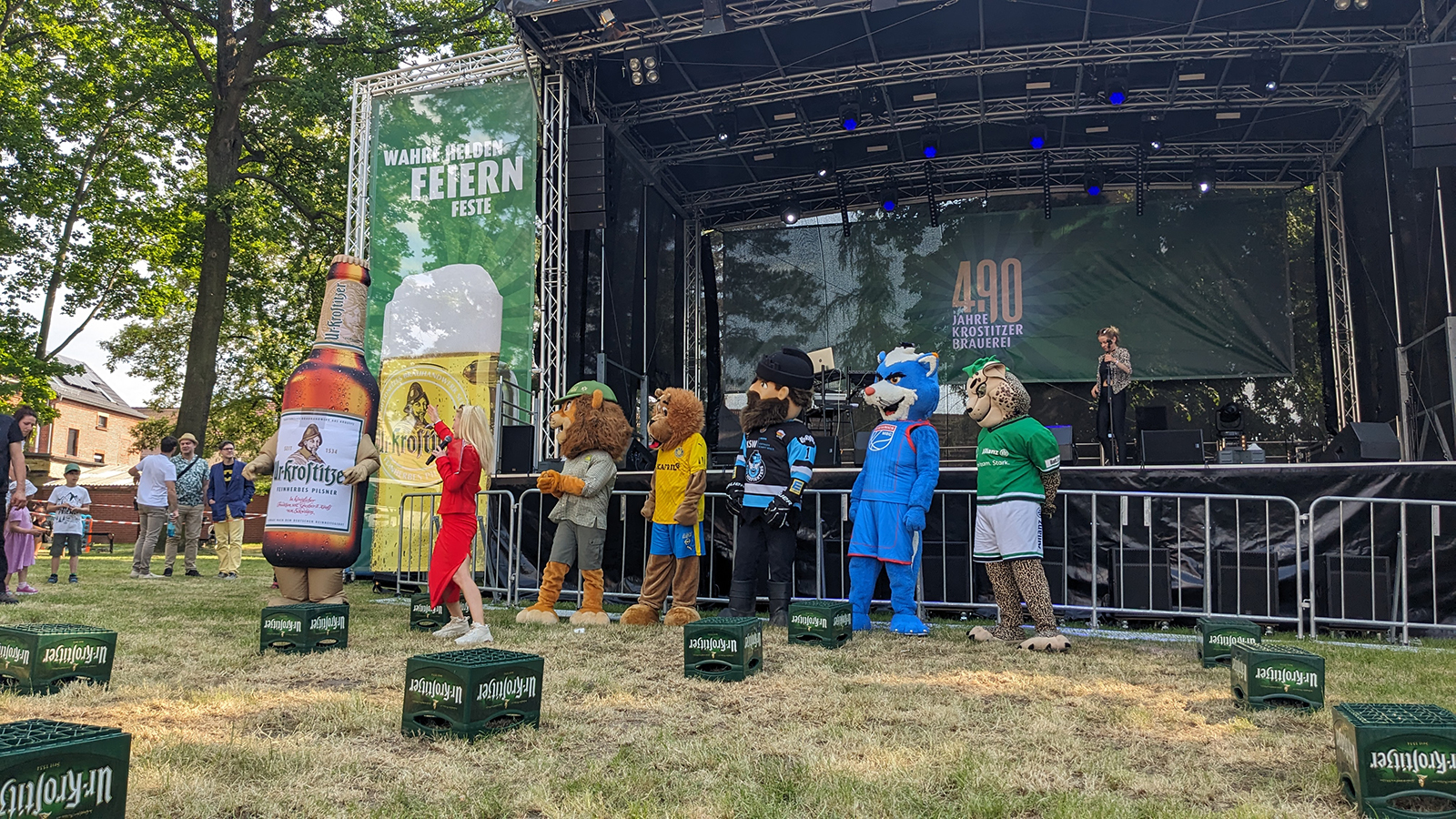 Mehrere Maskottchen stehen auf einer Bühne bei einem Outdoor-Festival.