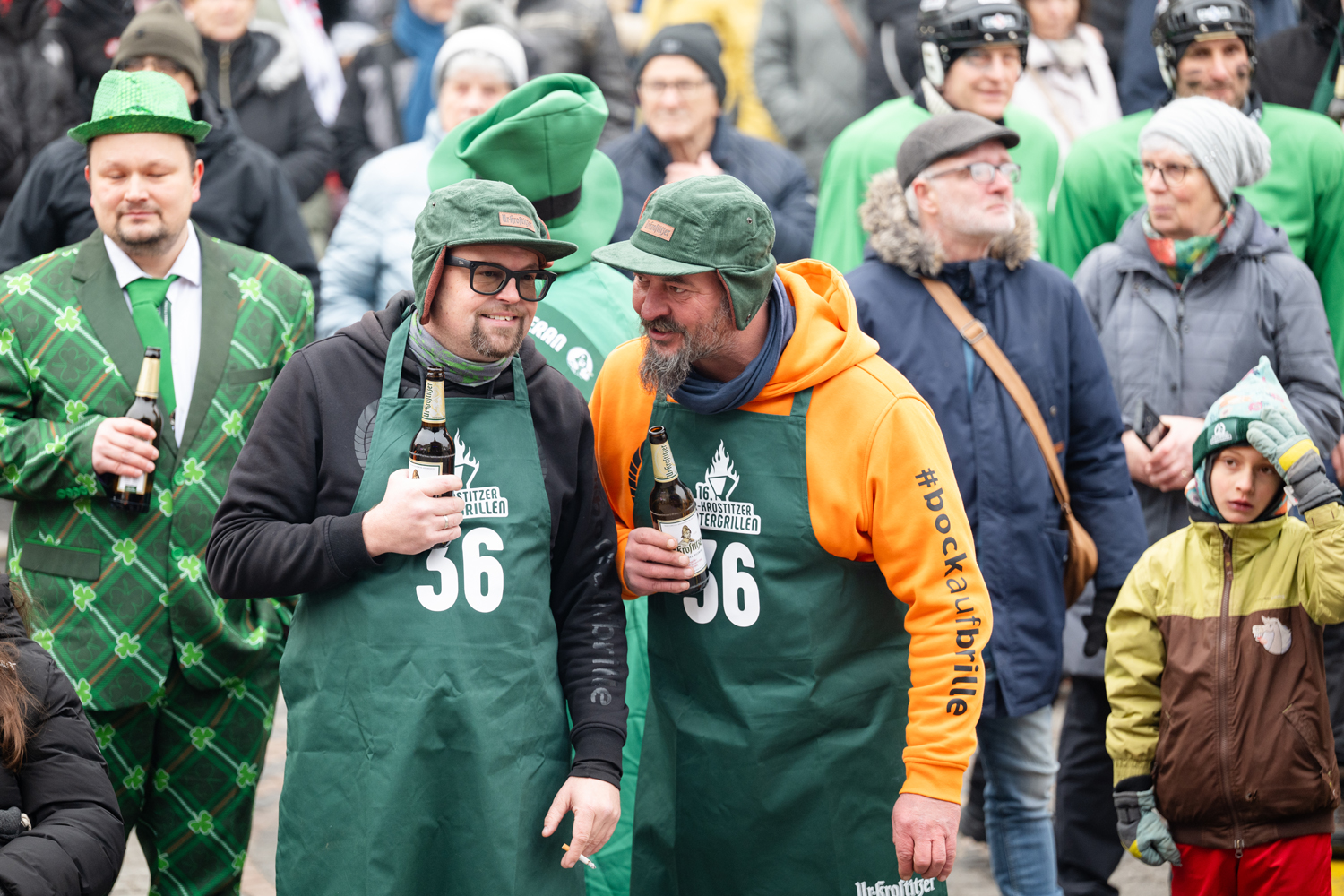 Zwei Personen mit Schürze und Bierflasche in der Hand in einer Menschenmenge
