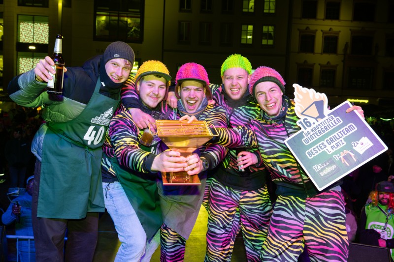 Eine Gruppe bunt gekleideter lachender Männer mit Pokal