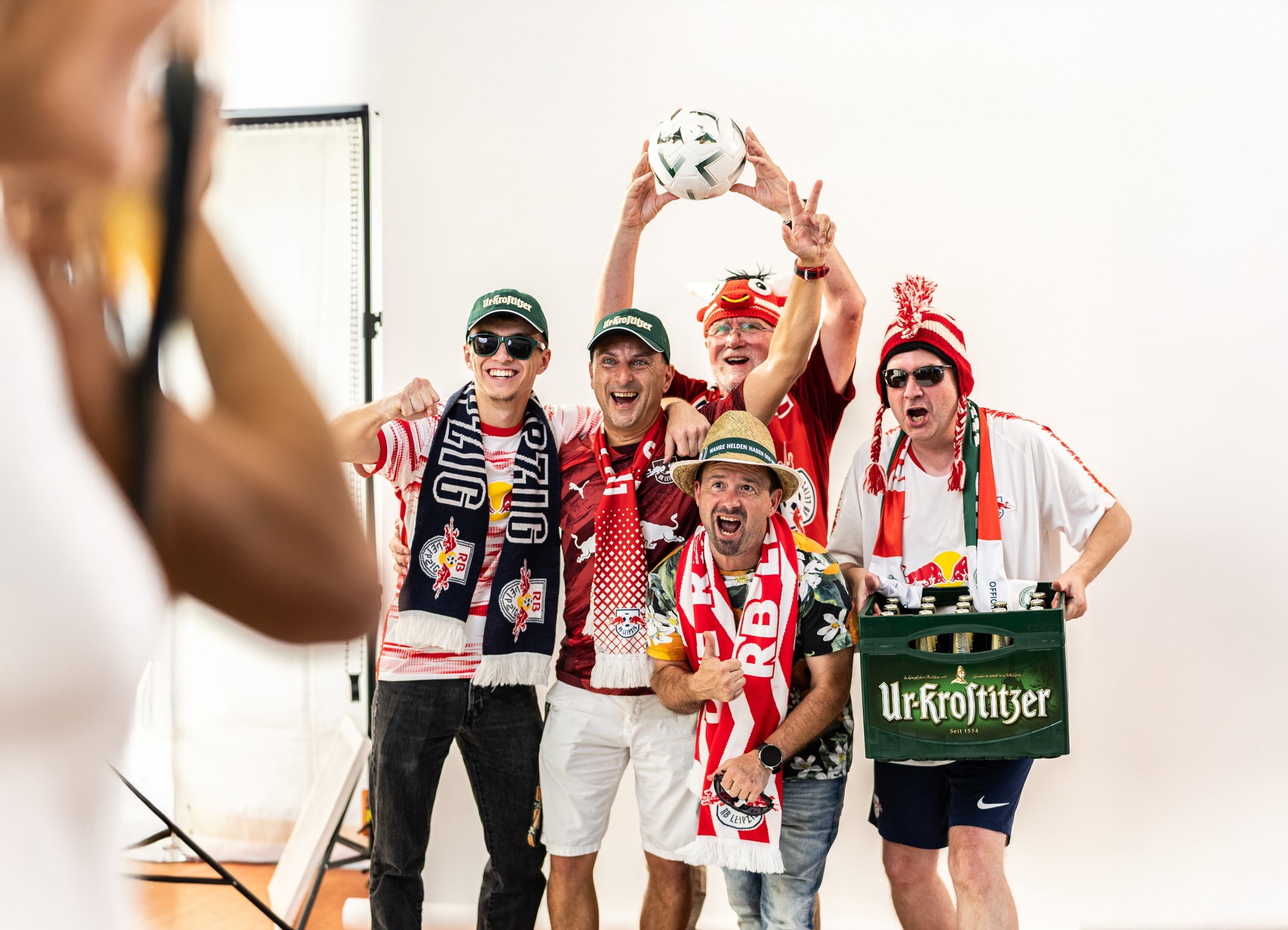 Fotoshooting einer Gruppe jubelnder Männer mit RB Leipzig-Fanartikeln und einer Kiste Ur-Krostitzer Bier.