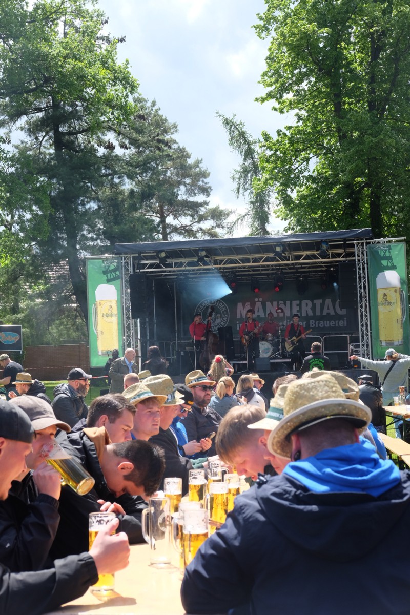 Eine Gruppe von Menschen sitzt an Festzelt Garnituren und feiert, auf der Bühne spielt eine Band.