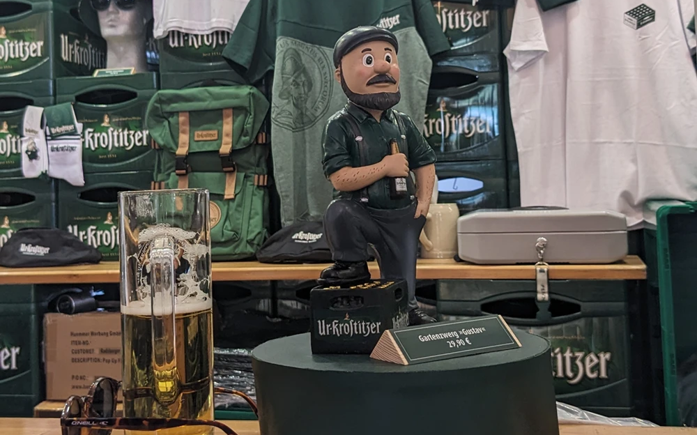Ein Ausstellungsstand zeigt grüne Kleidung und eine Figur neben einem Bierglas.