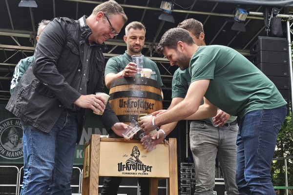 Fünf Männer stehen auf einer Bühne und stechen ein Fass BIer an.