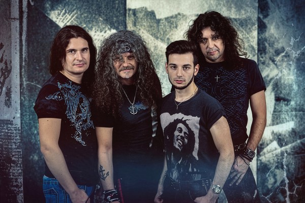 Vier Männer einer Band stehen nebeneinander vor einer grau gemusterten Wand.