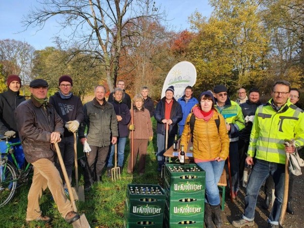 Gruppe von Leuten steht im Park mit Werkzeugen für eine Pflanzaktion.