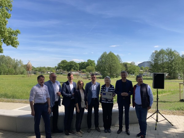 Neun Personen stehen nebeneinander in einem Park bei sonnigem Wetter.