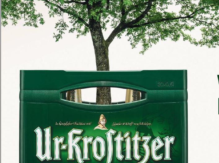 Ein grüner Getränkekasten steht vor einem Baum, auf dem Kasten ist ein Logo.