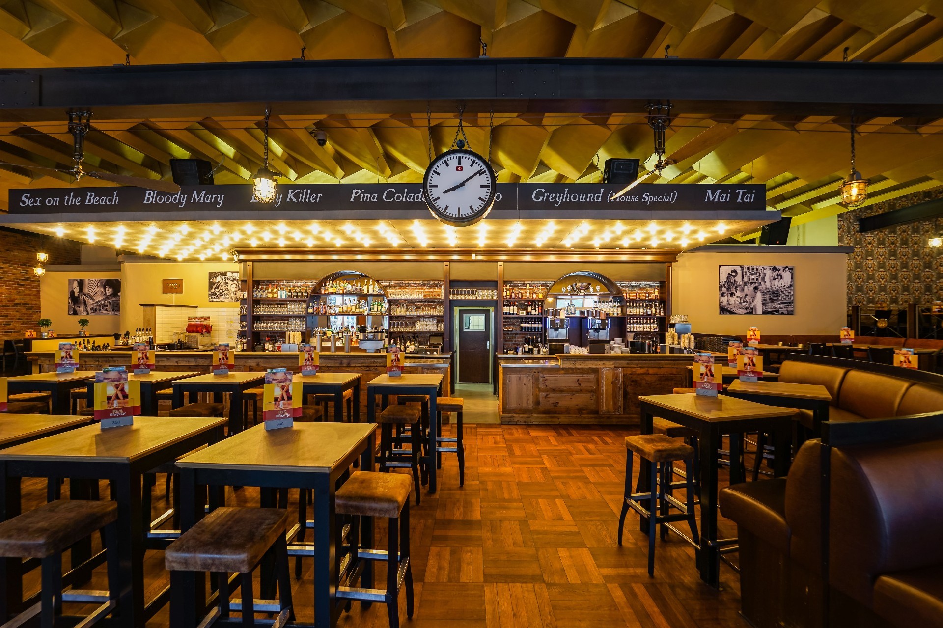 Innenansicht eines Restaurants mit Bar und verschiedenen Sitzbereichen, hellem Licht und Dekor.