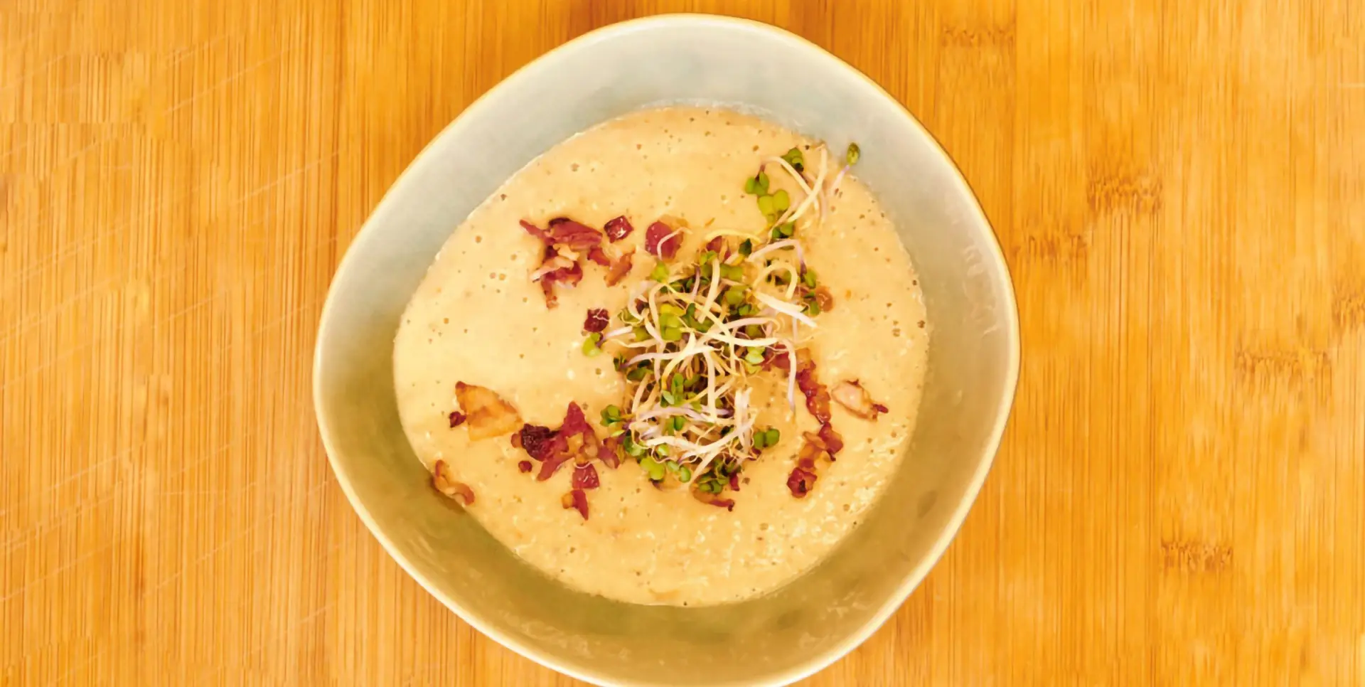 Eine Schüssel mit cremiger Suppe, garniert mit Speck und Sprossen.