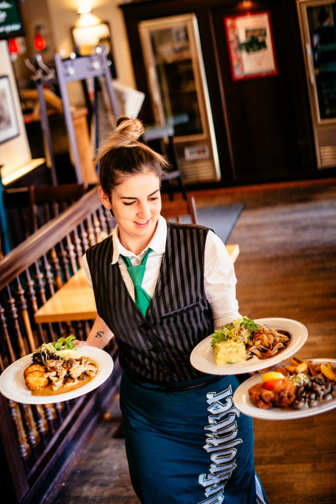 Eine Kellnerin trägt drei Teller mit Essen in einem Restaurant.