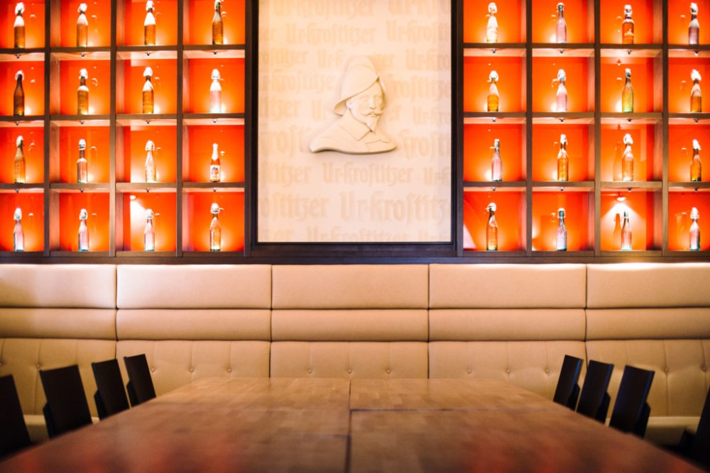 Ein langer Tisch steht vor einer Wand mit beleuchteten Regalen voller Flaschen.