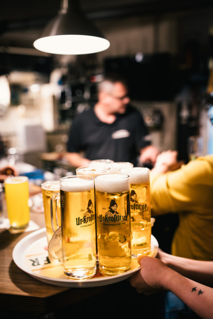 Eine Person trägt ein Tablett mit fünf Biergläsern in einer Bar.