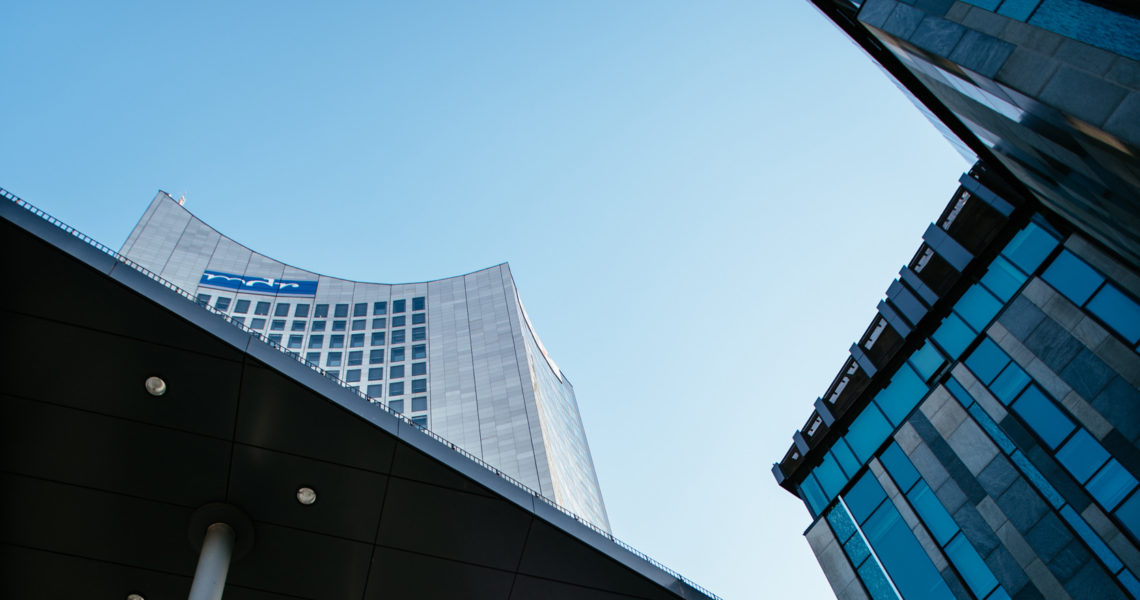 Ein Blick nach oben zeigt moderne Hochhäuser mit Glasfassaden unter klarem blauem Himmel.