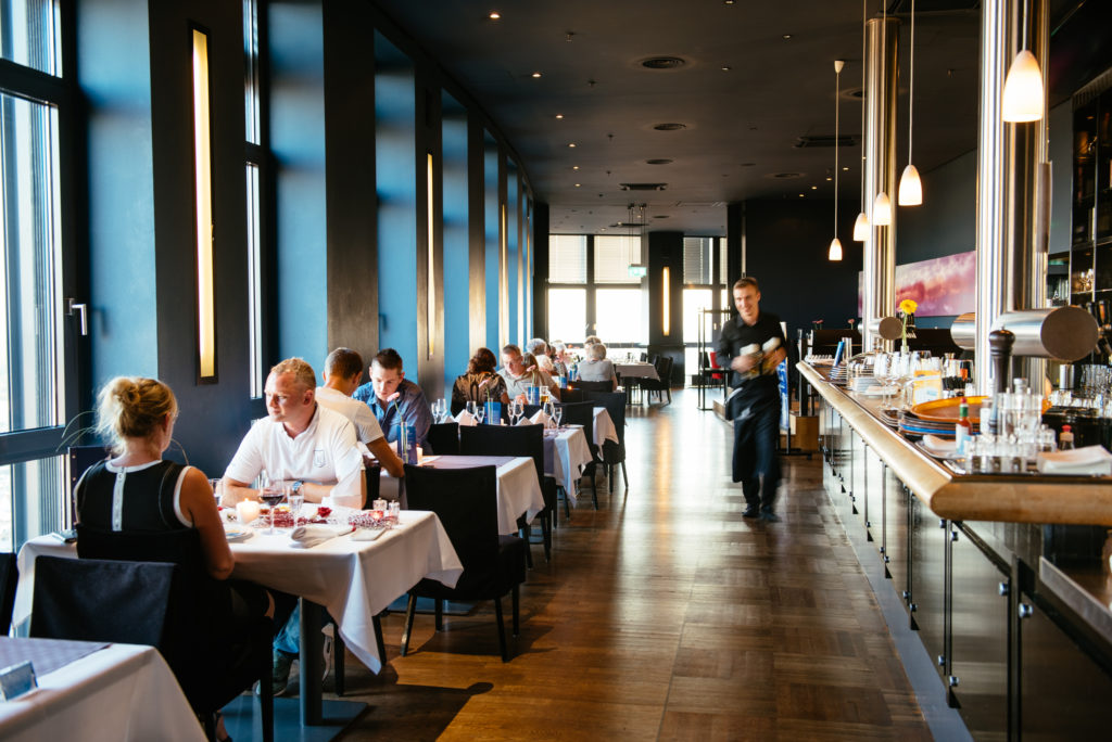 Ein Restaurant mit Gästen an Tischen und einem Kellner, der Geschirr trägt.