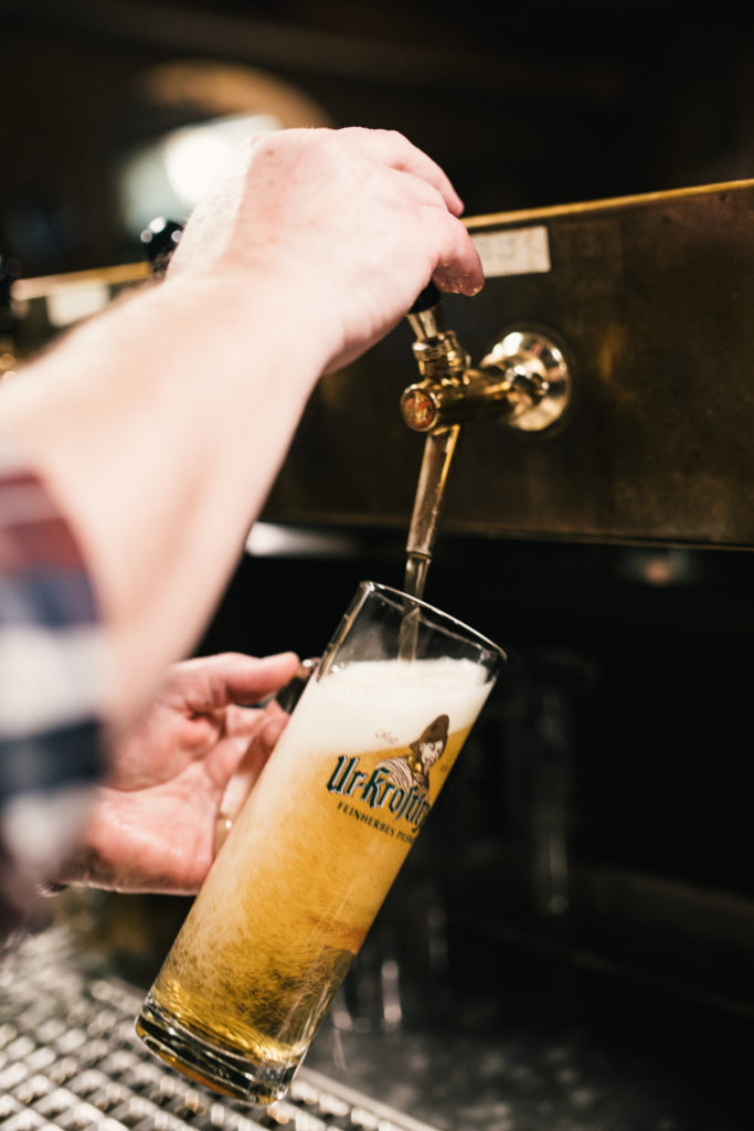 Eine Person zapft ein helles Bier in ein großes Glas an einer Bar.