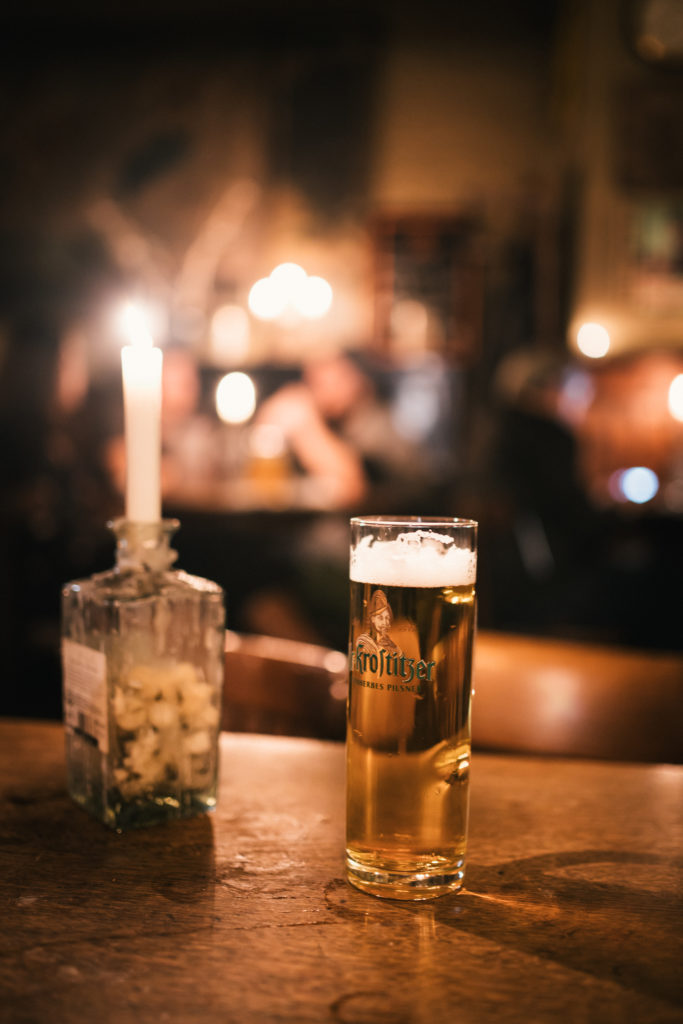 Ein Glas Bier steht auf einem Holztisch neben einer brennenden Kerze in einer gemütlichen Bar.
