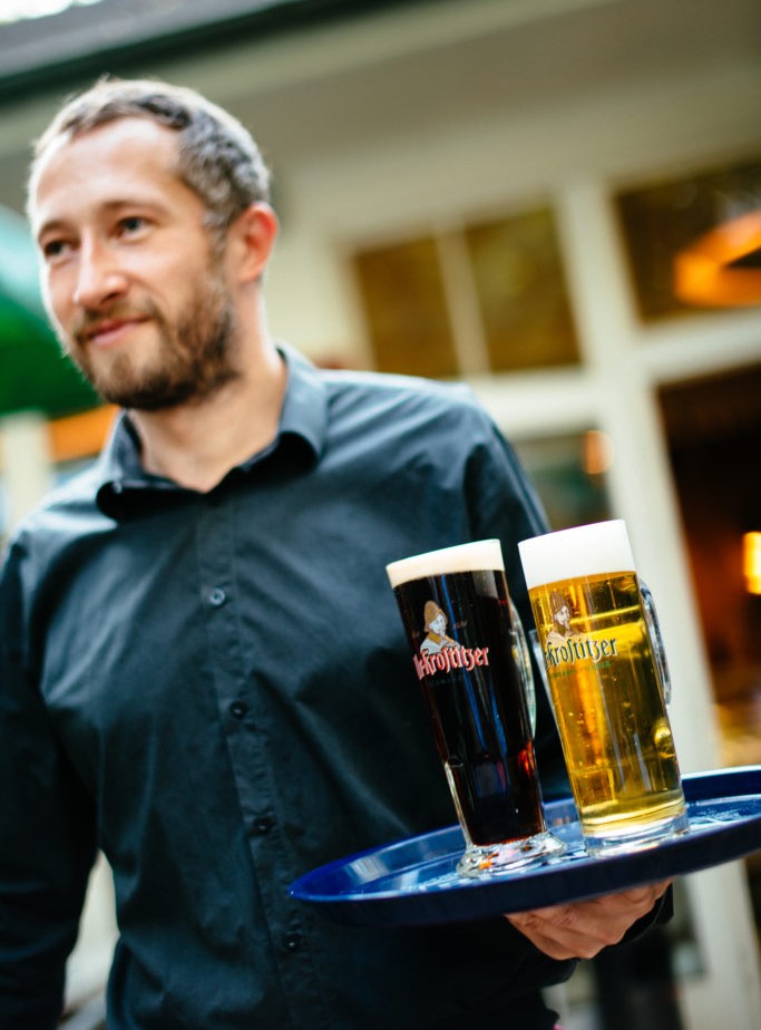 Ein Mann in einem schwarzen Hemd trägt ein Tablett mit zwei Biergläsern.