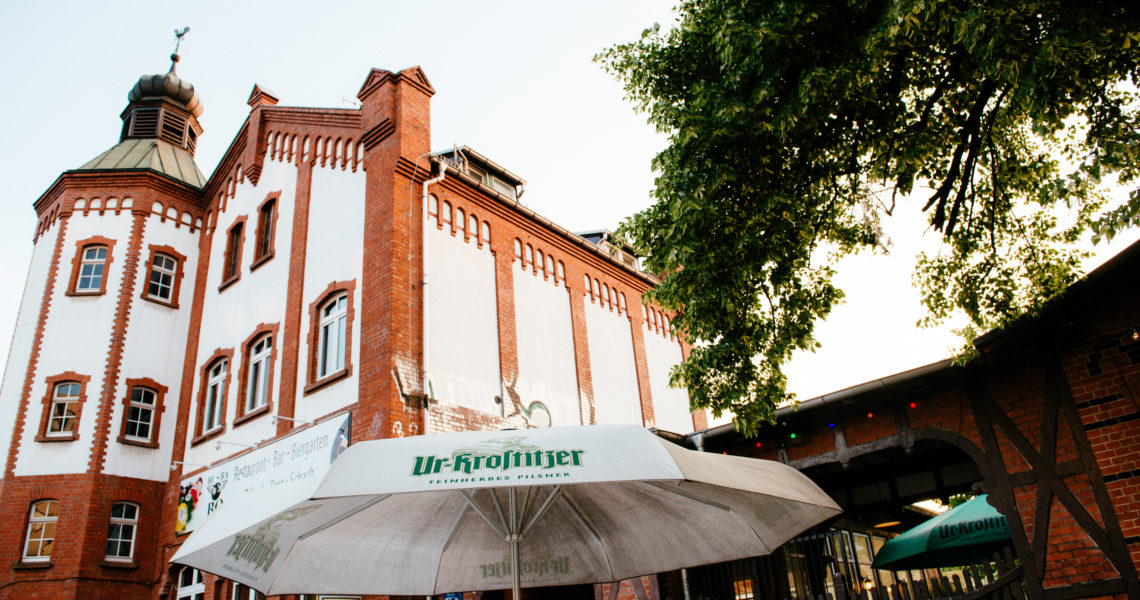 Zwei Regenschirme stehen vor einem historischen Backsteingebäude mit Türmchen.