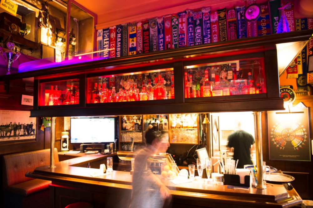 Eine belebte Bar mit vielen Flaschen im Regal und leuchtenden Neonlichtern.