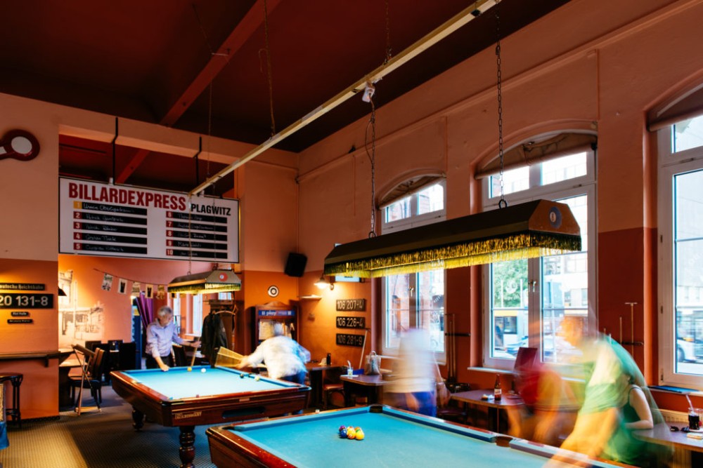 Innenansicht einer belebten Billardhalle mit mehreren Personen, die spielen.