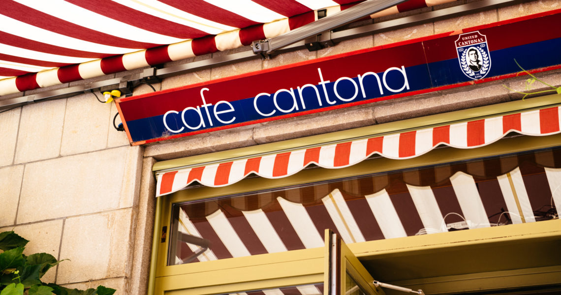 Ein Café-Eingang mit gestreifter Markise und passendem Schild darüber in Rot und Blau.