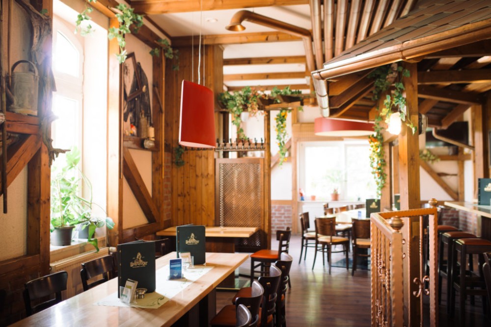 Gemütliches Restaurantinterieur mit Holzmöbeln und hängenden Pflanzen. Natürliches Licht flutet durch große Fenster.