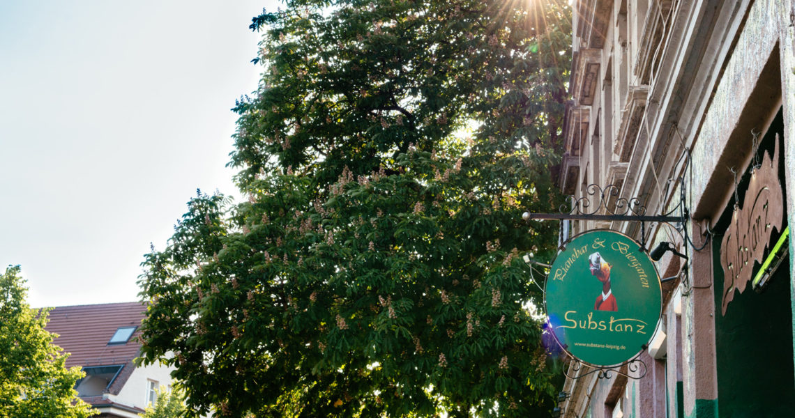 Sonnenstrahlen scheinen durch die Blätter eines großen Baumes neben einem Geschäftsschild.