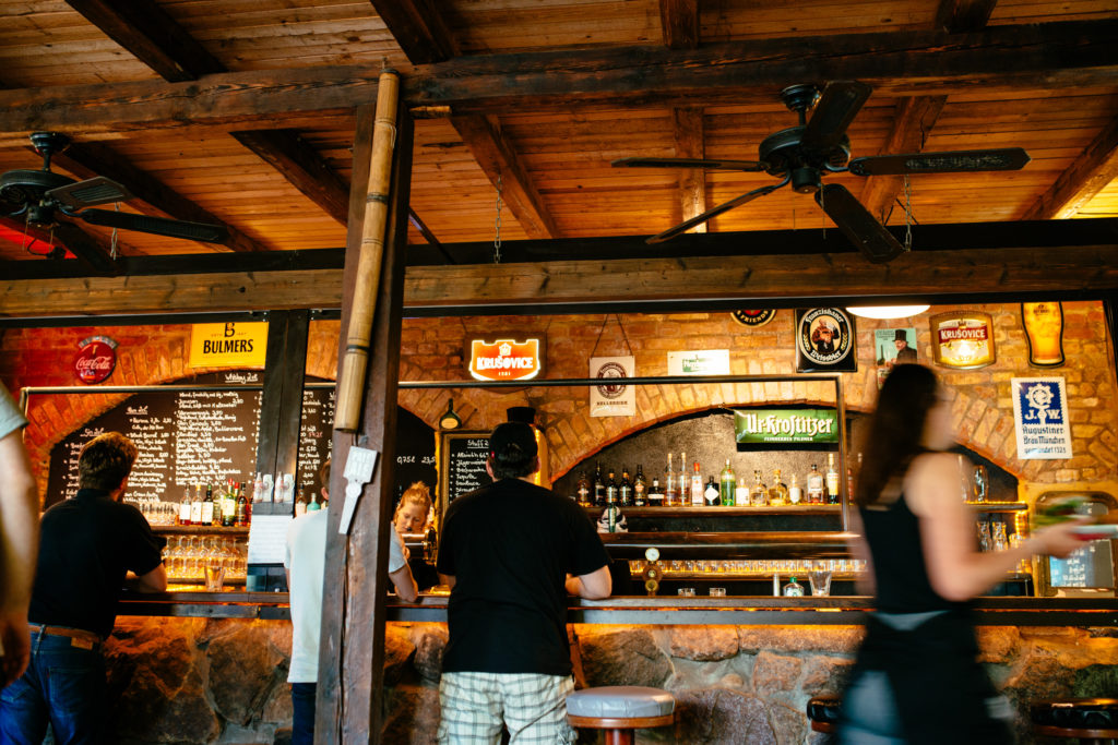 Drei Personen stehen an einer gut beleuchteten Holzbar in einem rustikalen Ambiente.