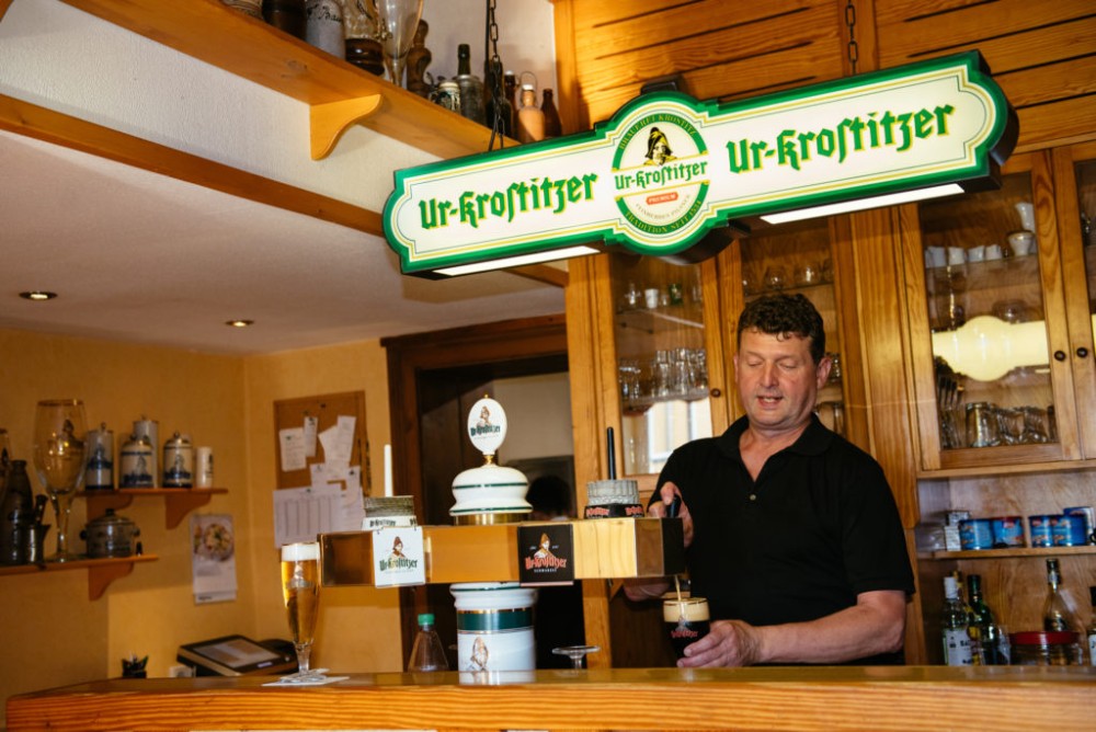 Ein Mann steht hinter einem Tresen und zapft ein helles Bier in ein Glas.