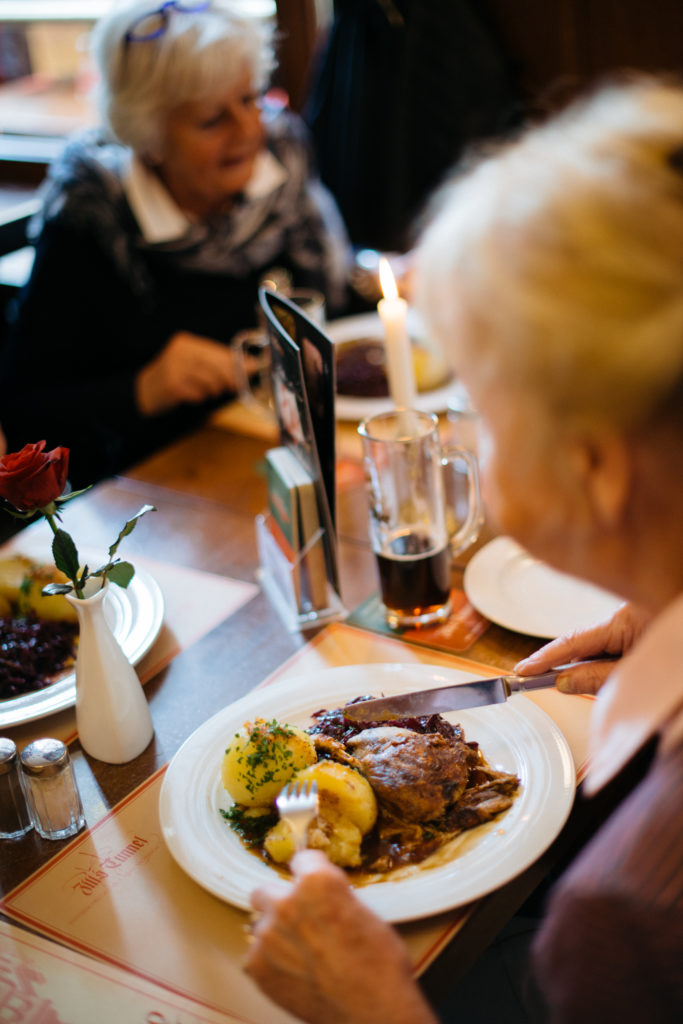 Eine ältere Dame isst in einem belebten Restaurant eine Mahlzeit mit Kerzenlicht.