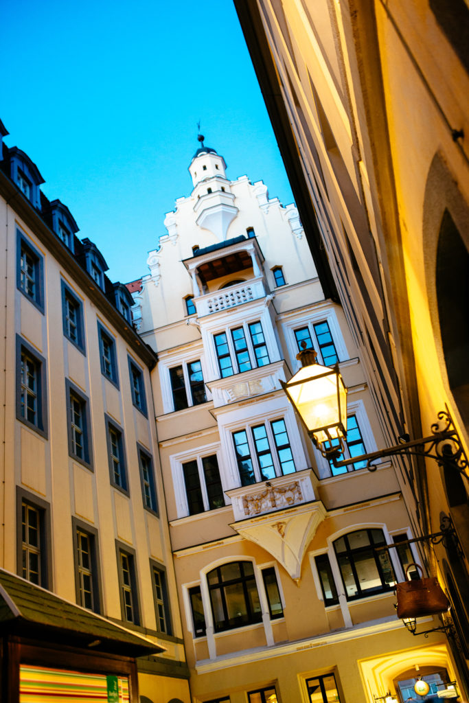 Historisches Gebäude mit weißen Verzierungen wird in einer Gasse bei Abendlicht beleuchtet.