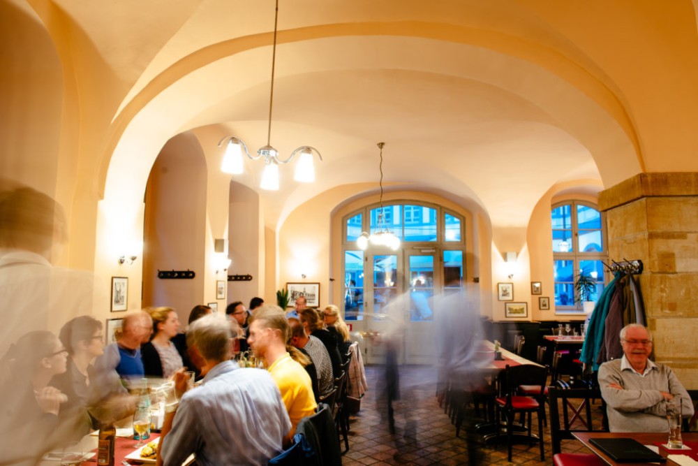 Gäste sitzen an Tischen in einem belebten Restaurant mit Gewölbedecken und warmem Licht.