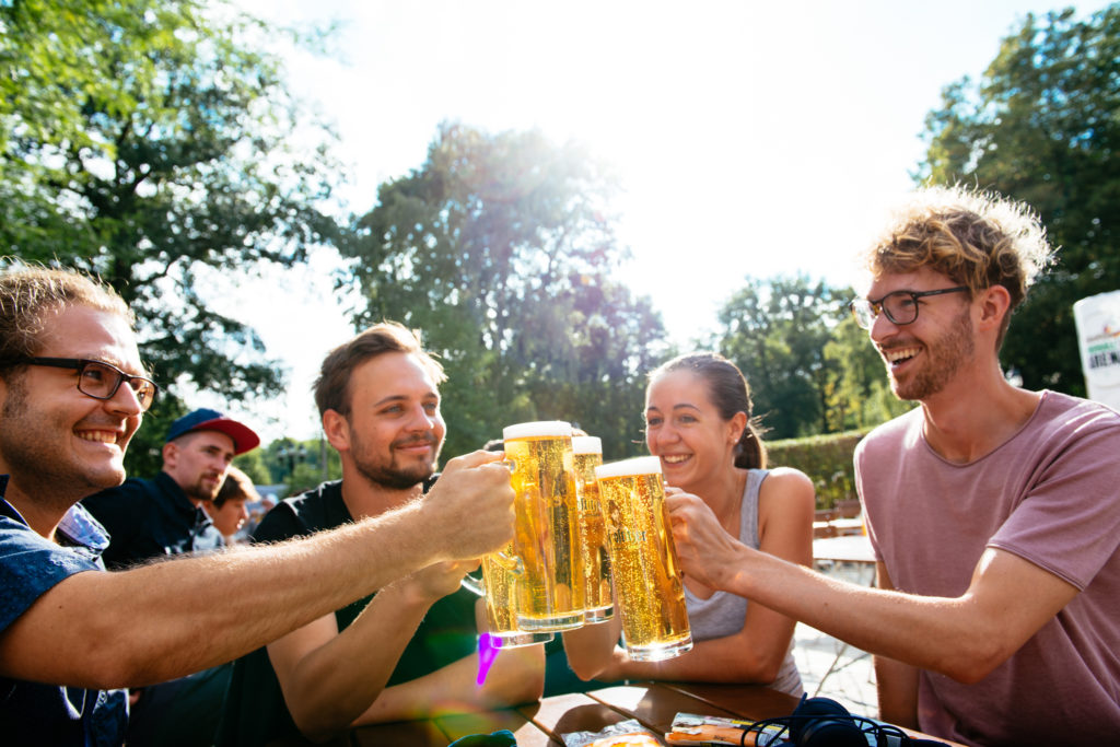 Vier Freunde stoßen im Freien mit Biergläsern an und lächeln.