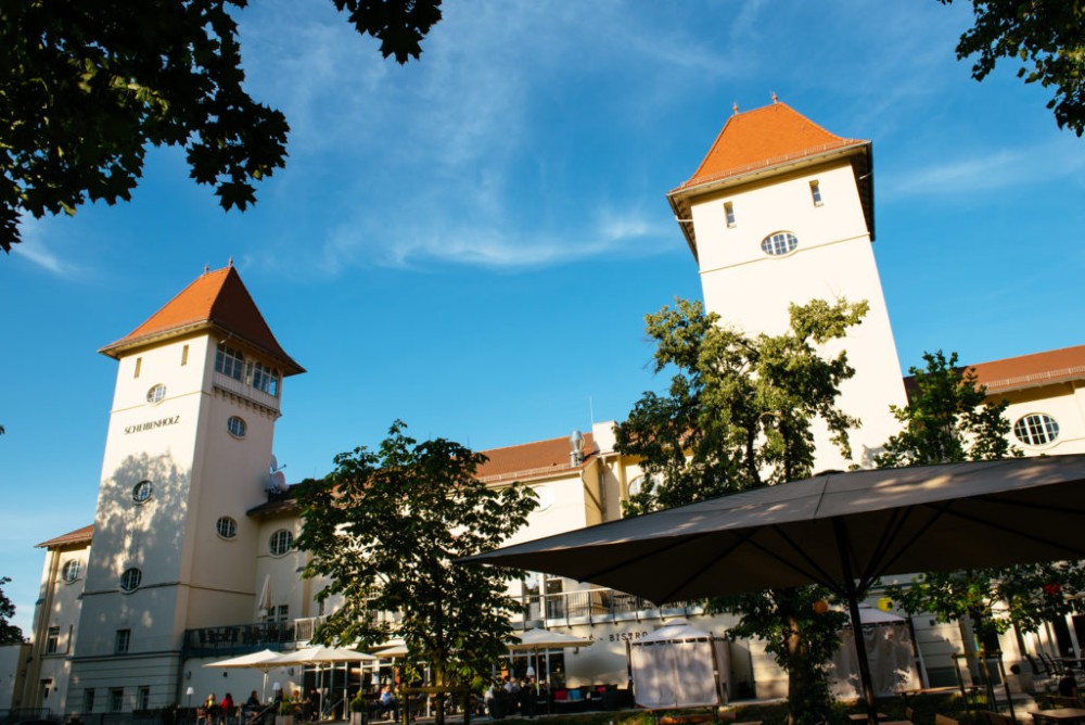 Ein großes Gebäude mit zwei Türmen steht unter blauem Himmel, umgeben von Bäumen.