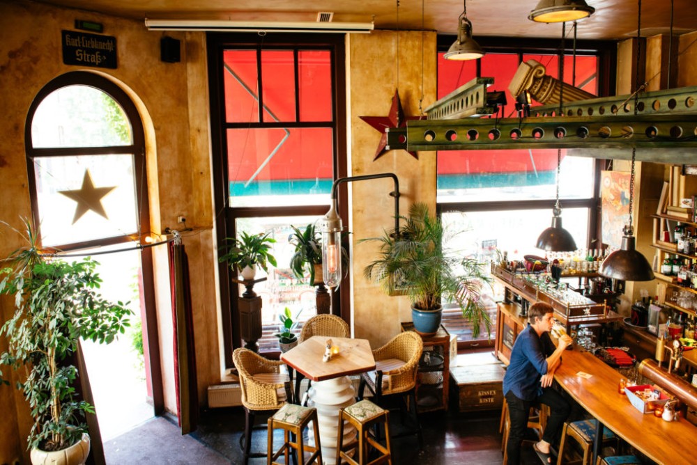 Ein Mann sitzt an einer Bar in einem gemütlich eingerichteten Café mit Pflanzen und Vintage-Dekor.