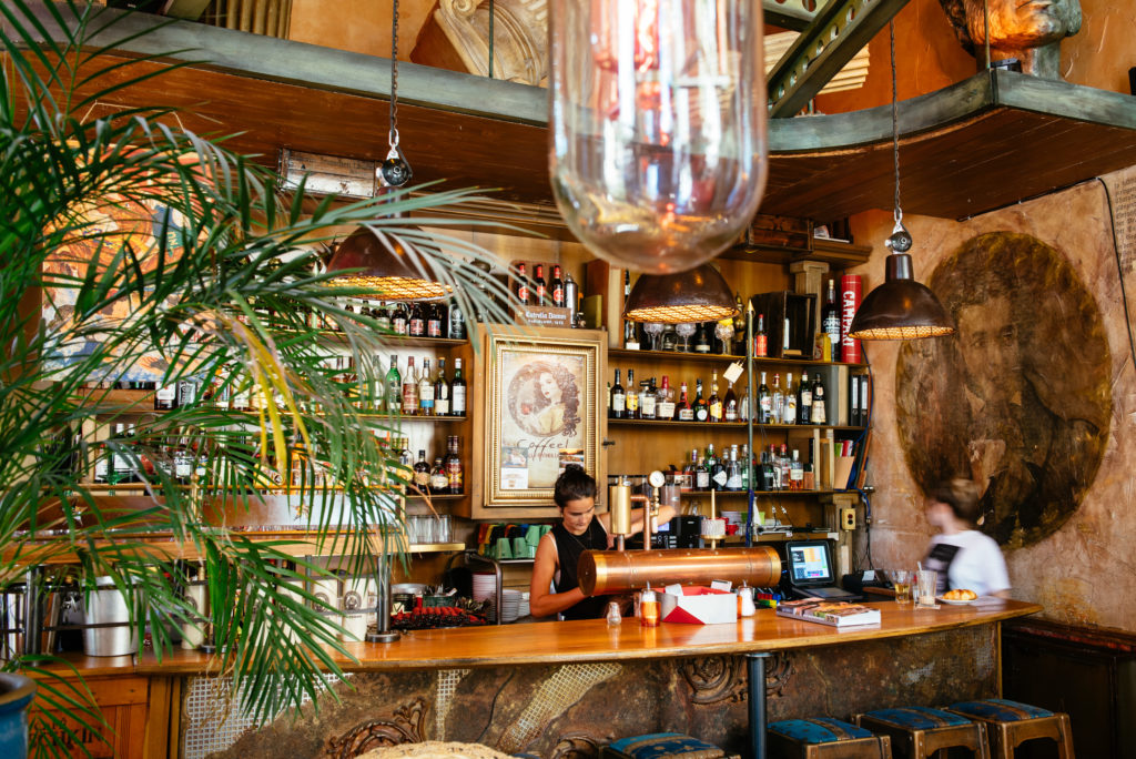 Eine Frau arbeitet konzentriert hinter der Bar eines rustikal eingerichteten Cafés.