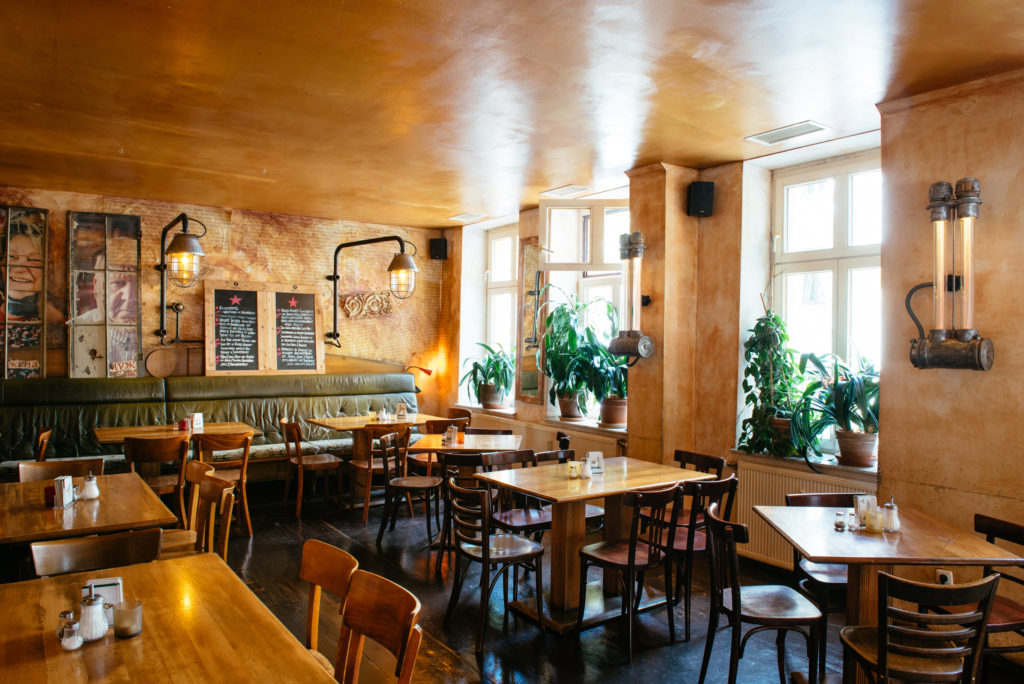 Ein gemütliches Café mit Holztischen und einer grünen Ledercouch unter einer beleuchteten Tafel.