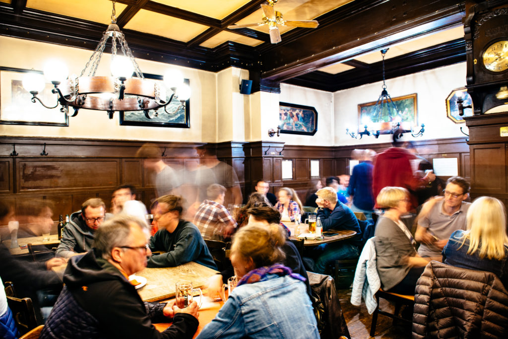 Menschen sitzen in einem belebten Gasthaus und unterhalten sich bei Getränken.