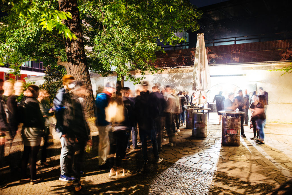 Menschen stehen bei Nacht draußen, die Bewegungsunschärfe zeigt Geschäftigkeit.