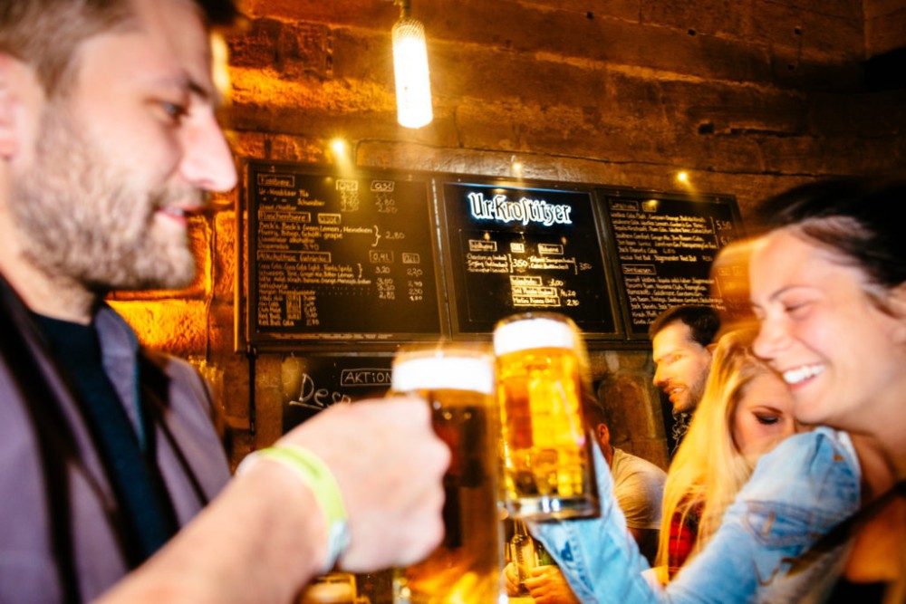 Ein Kellner reicht einer Frau lächelnd ein Bierglas in einer belebten Bar.