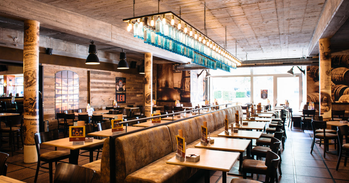 Innenansicht eines geräumigen Restaurants mit Holzelementen und blauen Flaschen als Lampen.
