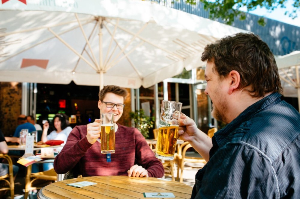 Zwei Männer prostet sich mit Biergläsern in einem Café im Freien zu.