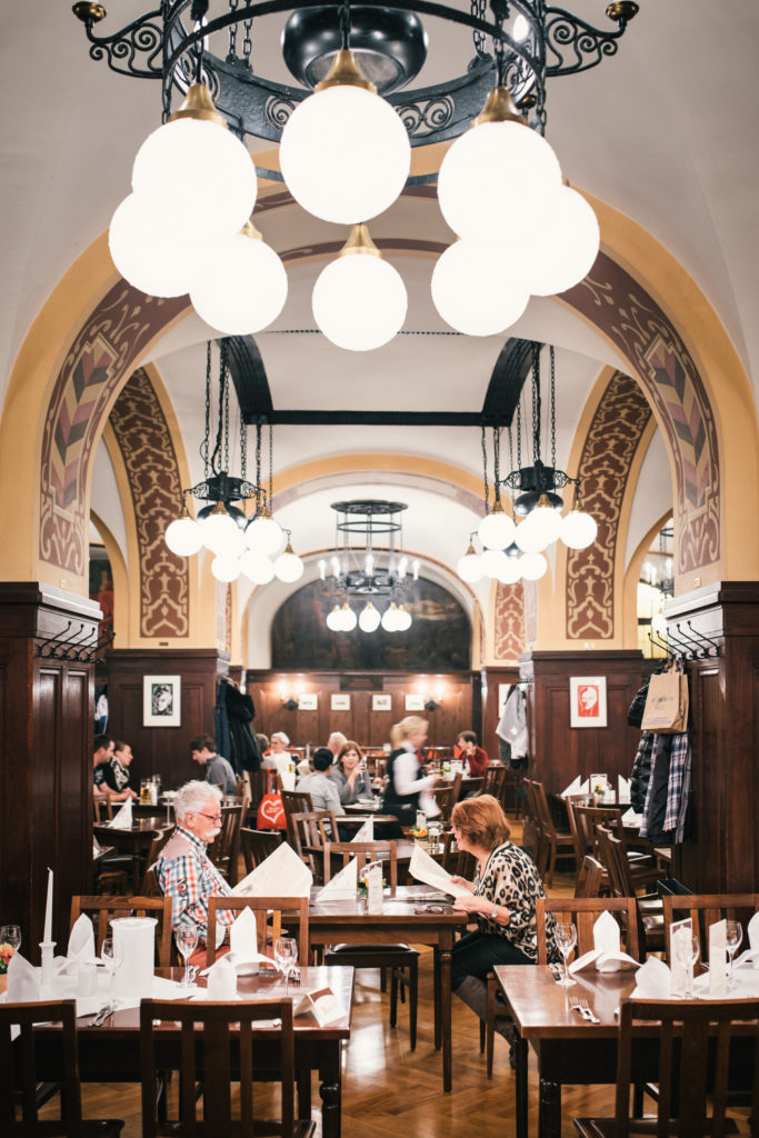 Menschen sitzen in einem geschäftigen Restaurant mit eleganten Bögen und Kronleuchtern.
