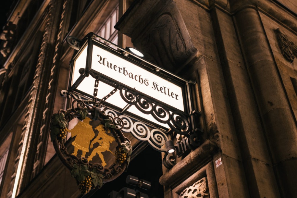 Beleuchtetes Schild an einem Gebäude zeigt „Auerbachs Keller“ und ein Wappen mit Figuren.