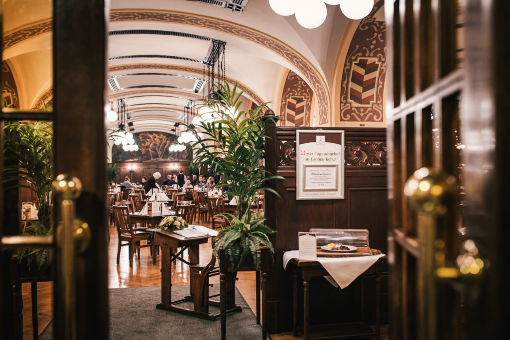 Elegantes Restaurantinterieur mit gewölbten Decken und vielen Gästen an Holztischen.