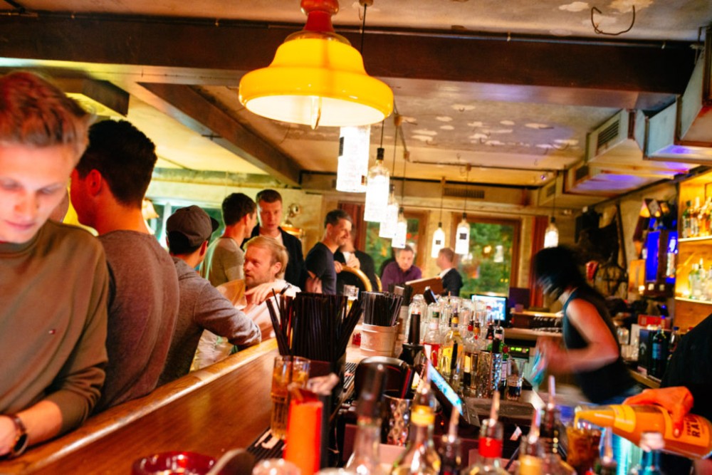 Menschen stehen an einer belebten Bar und unterhalten sich, während Getränke serviert werden.