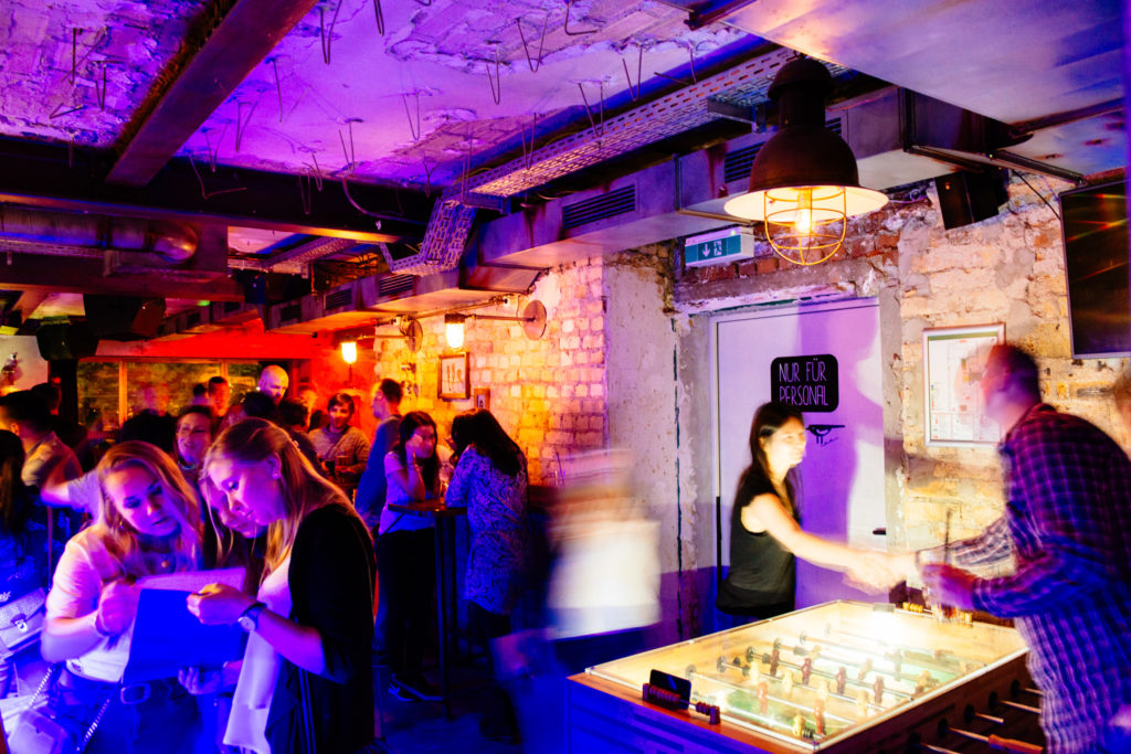 Lebendige Bar mit Personen, die beim Tischfußball spielen und im Gespräch sind.